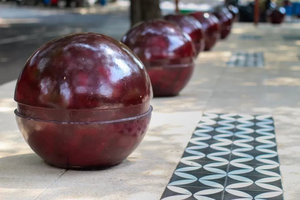 Red spherical bollards lining city sidewalk.